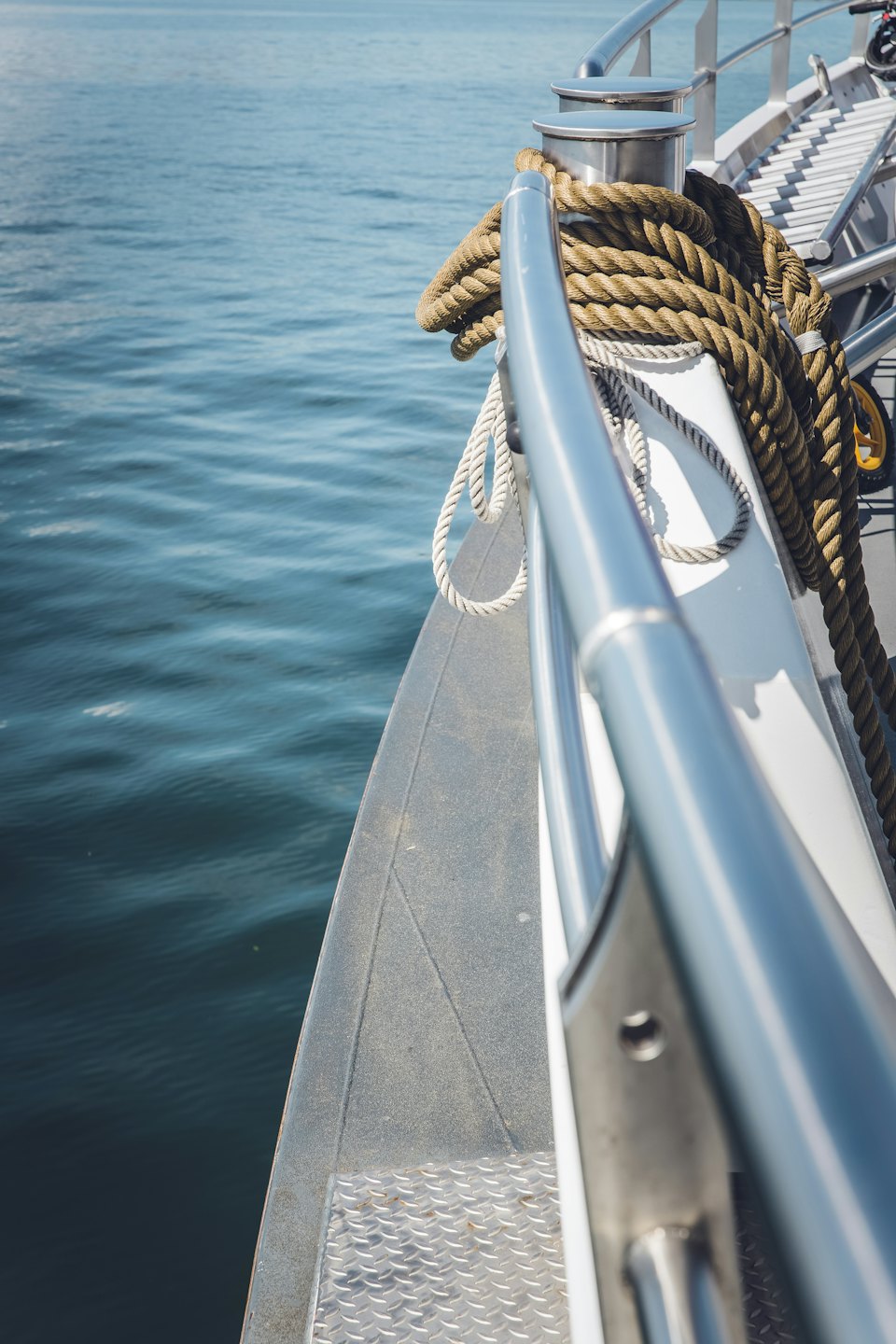 Looking down a stainless rail and coiled line to calm blue water alongside the hull.