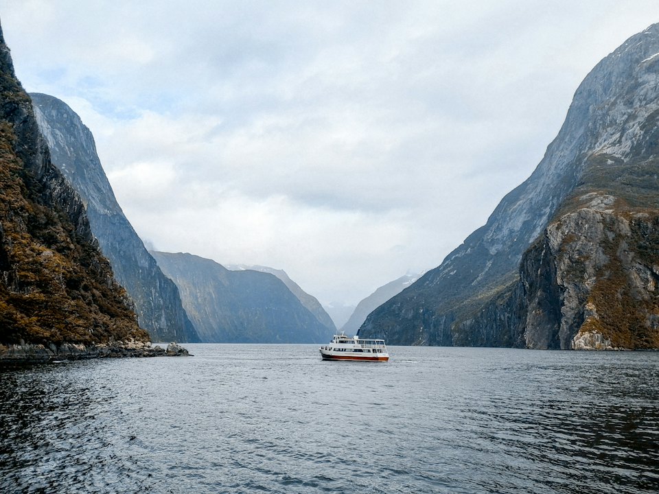 A small vessel underway in a vast fjord between steep cliffs.