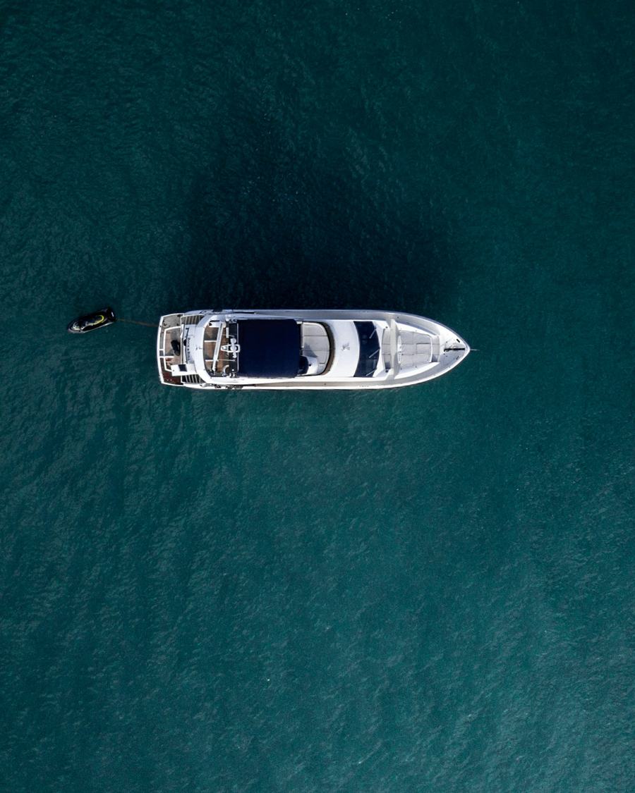 Aerial view of a motor yacht at anchor on calm, deep-teal water.