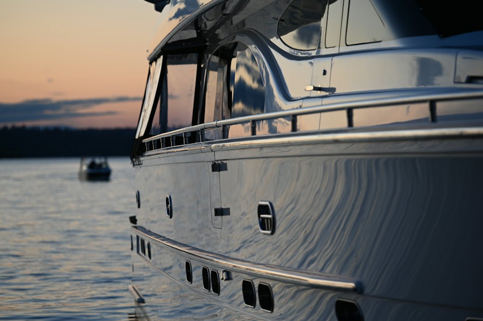 The polished flank of a motor yacht reflecting a calm harbor at dusk.
